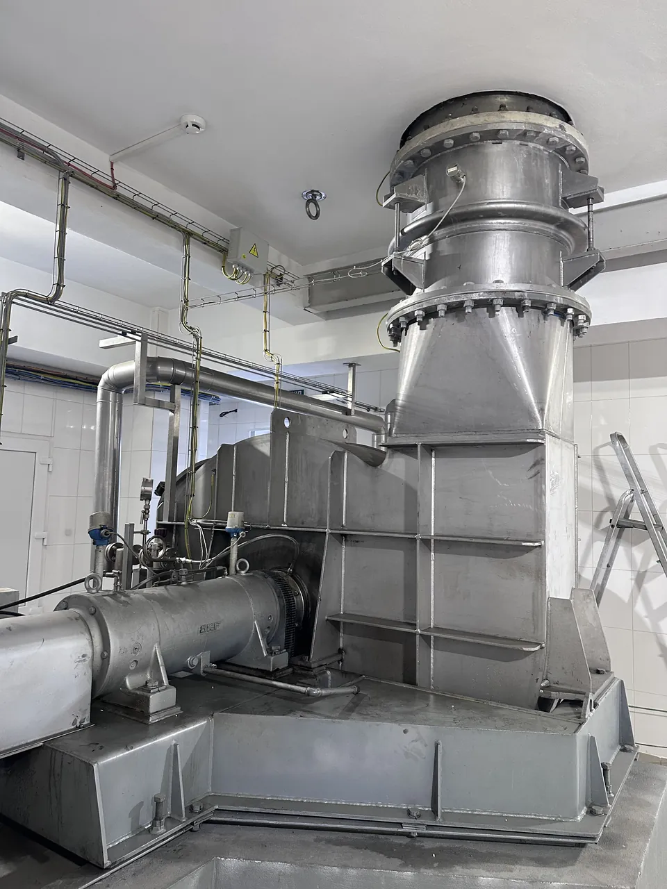 Bare stainless steel MVR fan casing with the vertical vapour duct and expansion joint rising to the ceiling